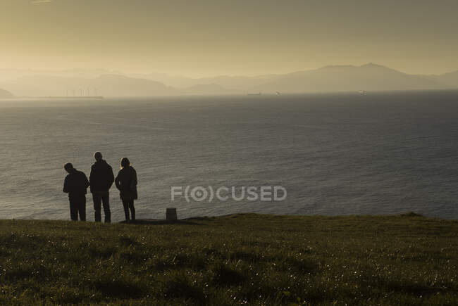Група мандрівників, що стоять на узбережжі мирного моря з гірським силуетом в ранковий час — стокове фото