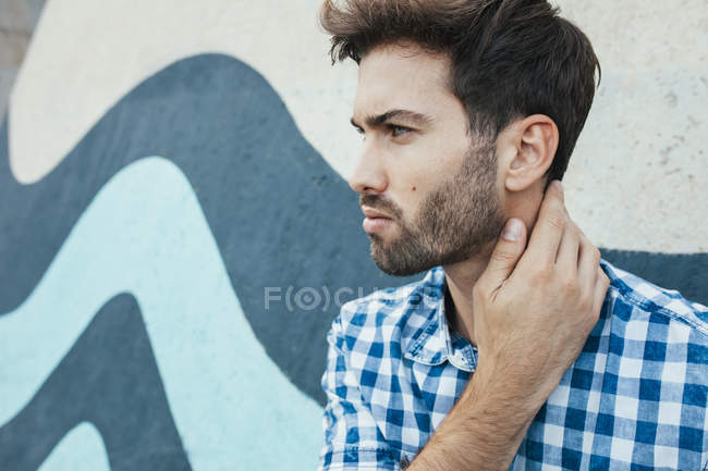 Cheerful young male in casual plaid shirt looking away with painted wall on background — Stock Photo
