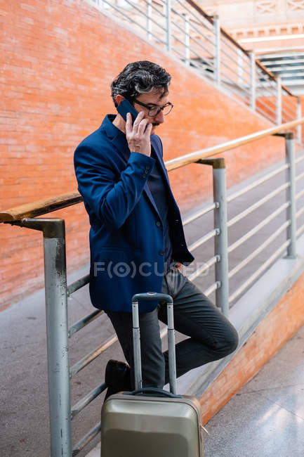 Uomo anziano in piedi con bagagli e parlare su smartphone — Foto stock
