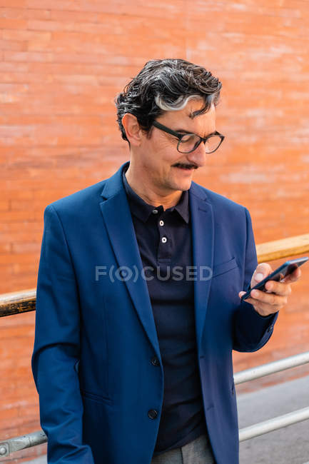 Homem de negócios maduro em casaco azul usando smartphone — Fotografia de Stock