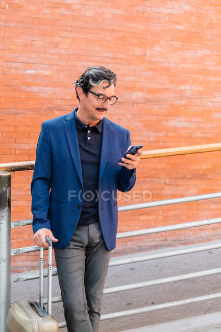 У віці чоловік стоїть з багажем і розмовляє по смартфону — стокове фото