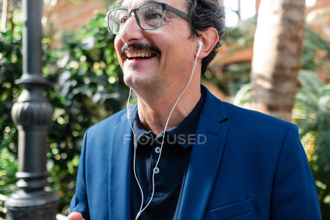 У віці бізнесмен використовує смартфон з навушниками та посміхається — стокове фото