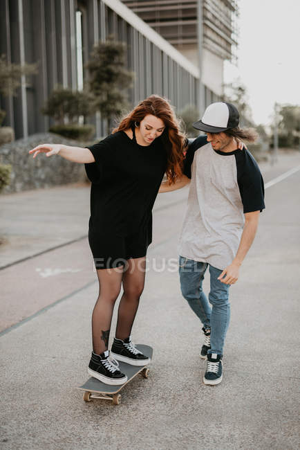 Rindo adolescente cara e menina aprendendo a patinar se divertindo na rua — Fotografia de Stock