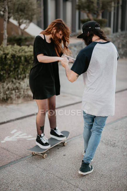 Сміється підліток хлопець і дівчина вчаться кататися на ковзанах розважаючись на вулиці — стокове фото