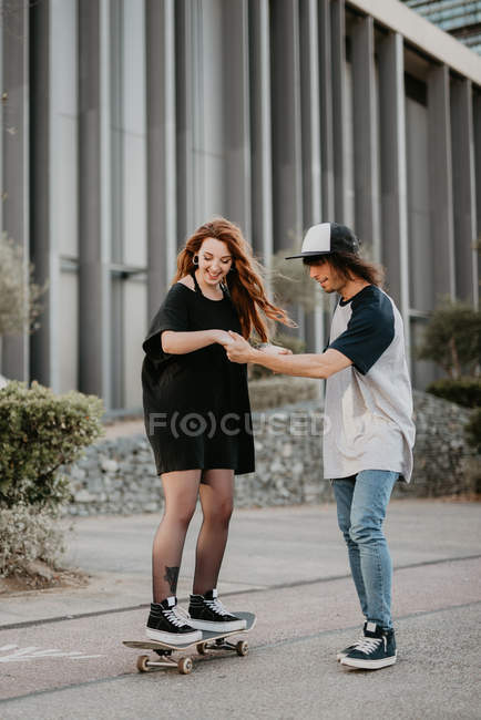 Laughing teenage guy and girl learning to skate having fun on street — Stock Photo