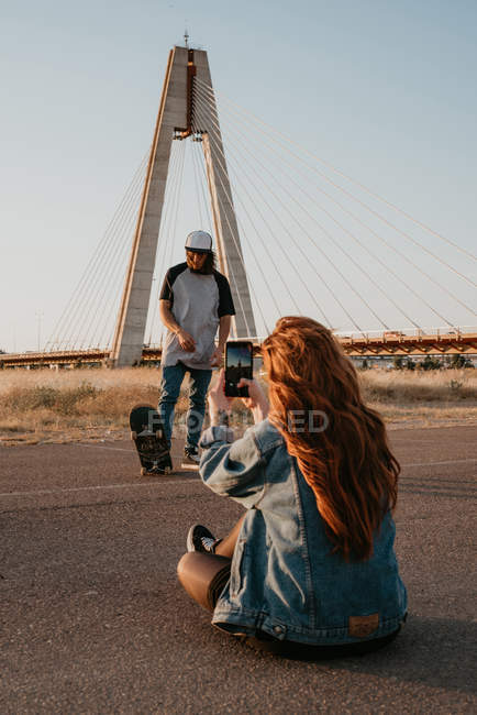 Casal adolescente na moda com skate na estrada remota vazia e tirar fotos com telefone celular — Fotografia de Stock