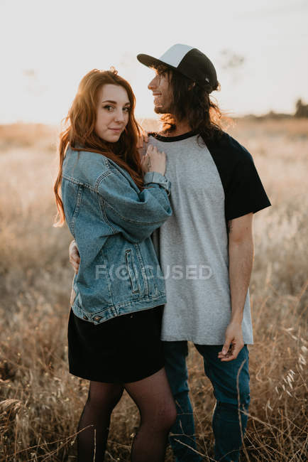 Jeunes adolescents élégants embrassant joyeusement wile debout dans un champ rural reculé avec la lumière du coucher du soleil chaud — Photo de stock