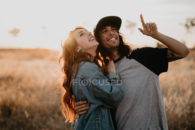 Jóvenes adolescentes elegantes abrazando felizmente astuto de pie en el campo rural remoto con luz cálida puesta del sol - foto de stock