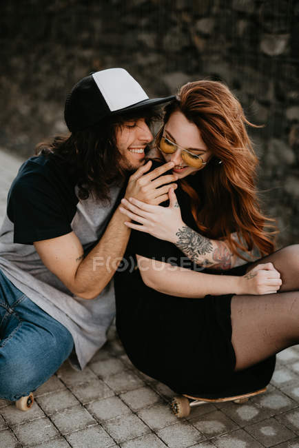 Cheerful cool trendy couple sitting on road with skateboard laughing with each other — Stock Photo
