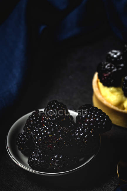 Tarta casera con moras y deliciosa crema de vainilla y menta con bol de bayas sobre fondo oscuro - foto de stock