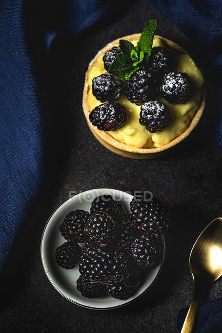 Tarta casera con moras y deliciosa crema de vainilla y menta con bol de bayas sobre fondo oscuro - foto de stock