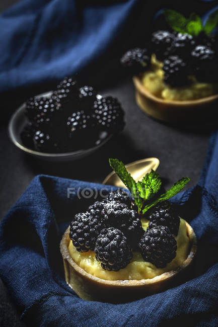 Домашні дрібні тістечка з ожиною та смачним кремом ванілі та м'ятою на темному фоні — стокове фото