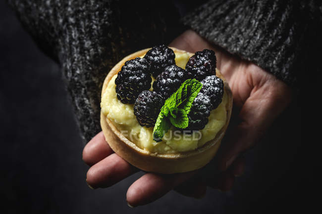 Persona irriconoscibile che tiene in mano una piccola torta fatta in casa con more e deliziosa crema di vaniglia e menta — Foto stock
