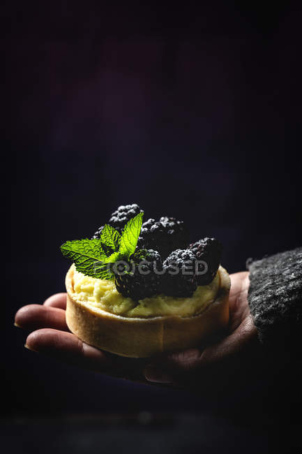 Persona irreconocible sosteniendo un pequeño pastel casero con moras y deliciosa crema de vainilla y menta - foto de stock