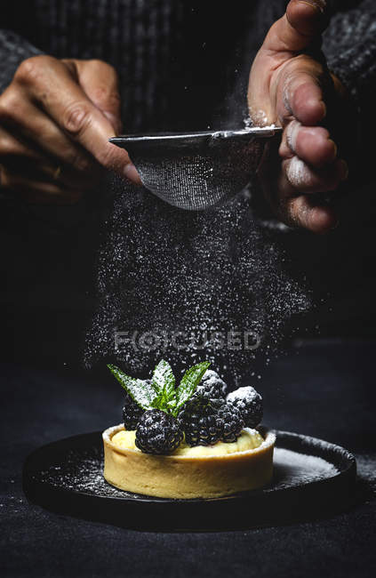 Unrecognizable person dusting powdered sugar over cake with blackberries and vanilla cream — Stock Photo