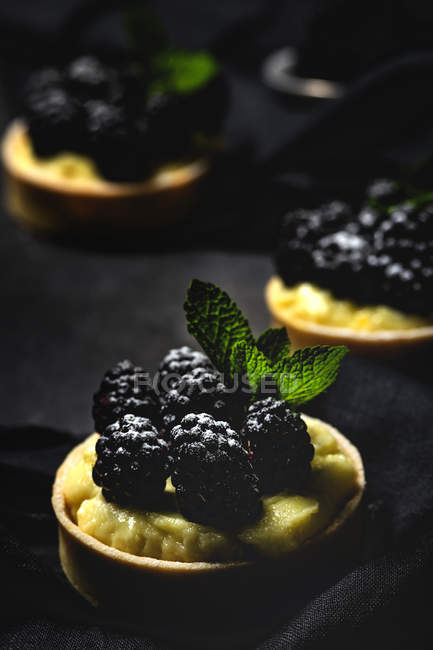 Primo piano di piccole torte fatte in casa con more e deliziosa crema di vaniglia e menta su sfondo scuro — Foto stock