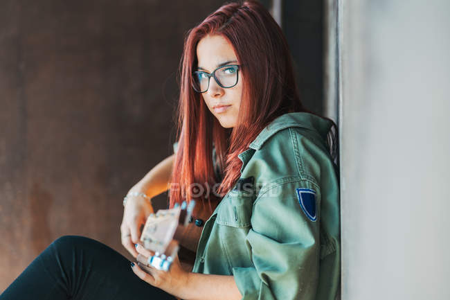 Side view of stylish content teenager thoughtfully playing guitar sitting on ground with crossed legs and looking at camera — Stock Photo