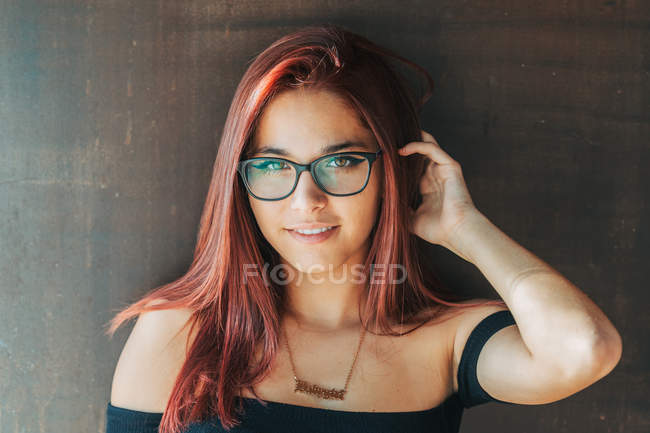 Conteúdo adolescente elegante em óculos nas proximidades parede marrom olhando para a câmera — Fotografia de Stock
