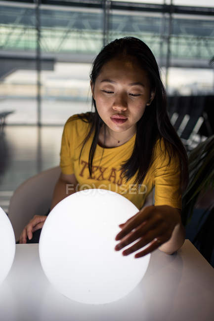 Cabelo comprido saído mulher asiática assistindo e tocando branco iluminando lâmpadas redondas na mesa no salão de espera — Fotografia de Stock