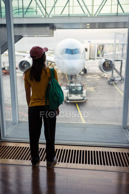 Vista trasera de una mujer irreconocible con gorra, mochila y ropa deportiva esperando en el aeropuerto - foto de stock