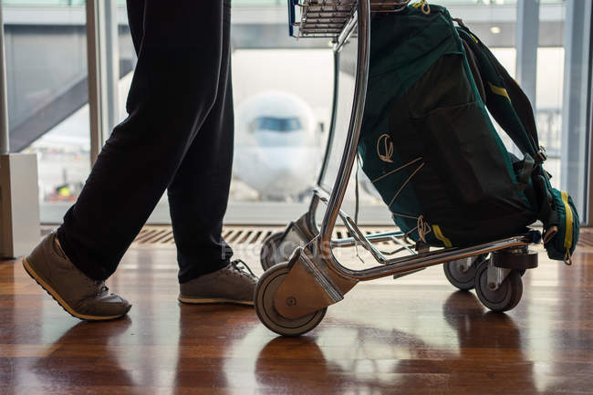 Обрезанный образ человека в спортивной одежде ходьба с багажом вдоль стульев в аэропорту — стоковое фото