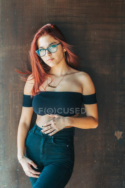 Stylish teenager in glasses and black t-shirt opening shoulders nearby brown wall looking at camera — Stock Photo
