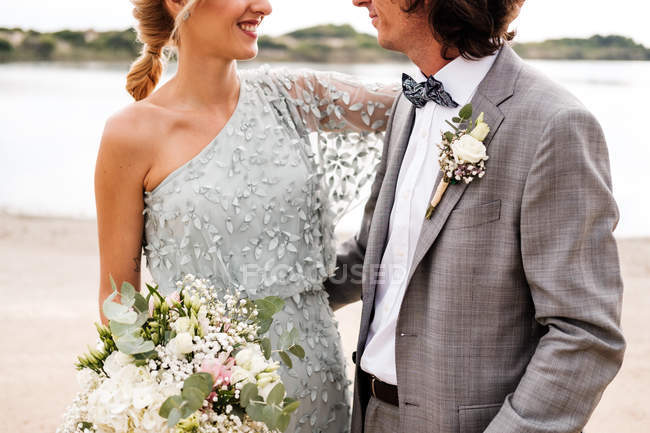 Обрізане зображення молодої пари в день весілля, що стоїть позаду порожнього піщаного узбережжя — стокове фото
