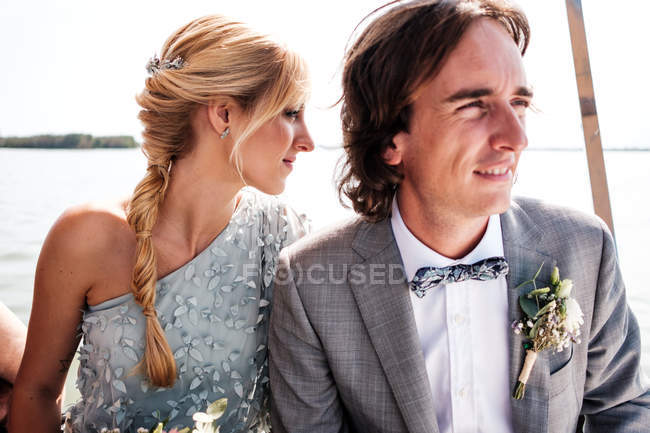 Zufriedene verheiratete Liebhaber in Hochzeitskleidung entspannen sich auf einem Boot mit Meer im Hintergrund — Stockfoto