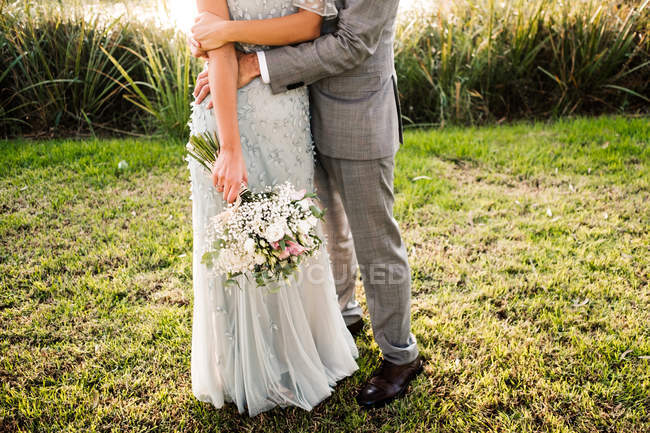 Cropped image of stylish newly married couple in wedded suits embracing each other on nature background — Stock Photo