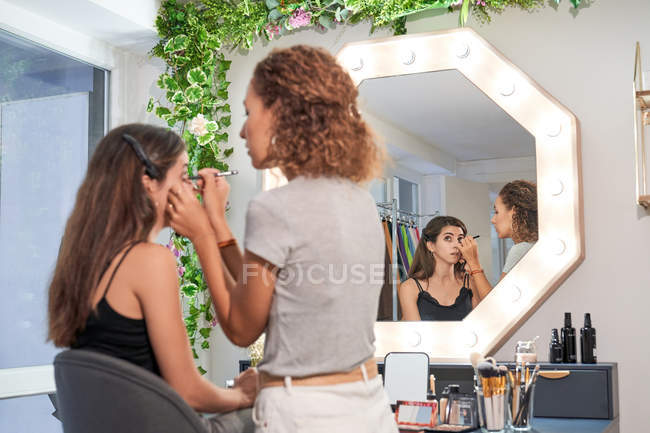 Side view of styist doing makeup for lady in chair in light stylish salon — стоковое фото