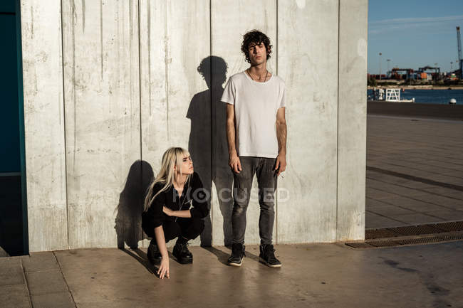 Woman in black clothes and shoes crouched beside tall relaxed man with cigarette standing with closed eyes — Stock Photo