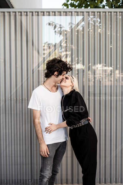 Вид збоку модна пара обіймає і цілує один одного, тоді як жінка спирається на хлопця проти смугастої стіни — стокове фото