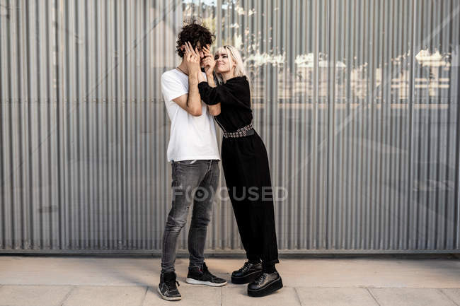 Vista lateral de pareja de moda jugando entre sí contra la pared rayada del edificio moderno - foto de stock
