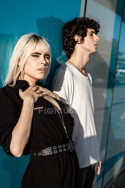 Жінка в чорному одязі стоїть поруч з високим чоловіком із закритими очима, стоячи на синій стіні з відображенням вулиці — стокове фото