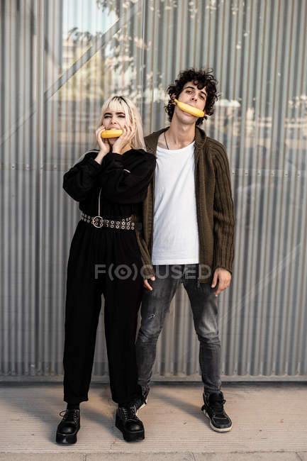 Homme et femme adultes à la mode extraordinaire tenant des bananes dans la bouche — Photo de stock