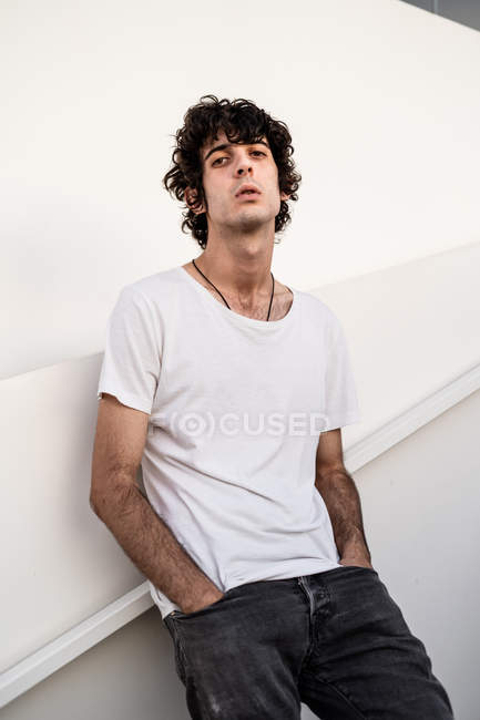 From below handsome confident dark haired man in casual clothes looking at camera against white wall — Stock Photo