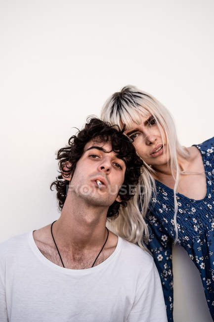 Jolie femme blonde et homme avec cigarette dans la bouche en regardant la caméra sur fond de mur blanc — Photo de stock