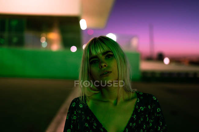 Attraktive selbstbewusste blonde Frau, die interessiert in die Kamera blickt, während sie im Morgengrauen allein auf der Straße steht — Stockfoto