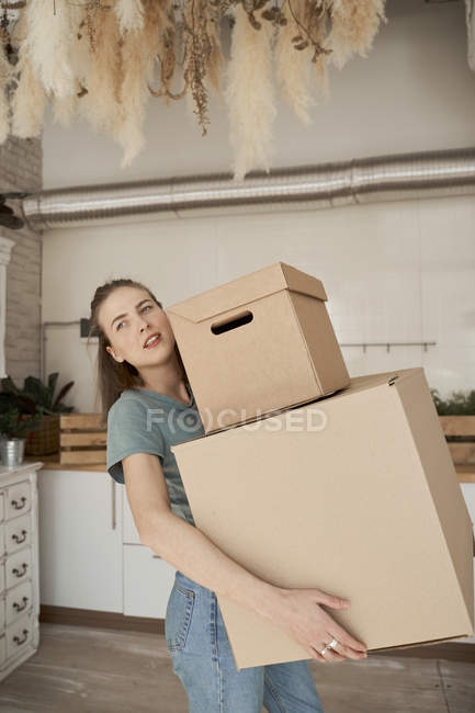 Seitenansicht einer jungen Frau, die sich bemüht und Pappkartons mit Sachen im Haus trägt — Stockfoto