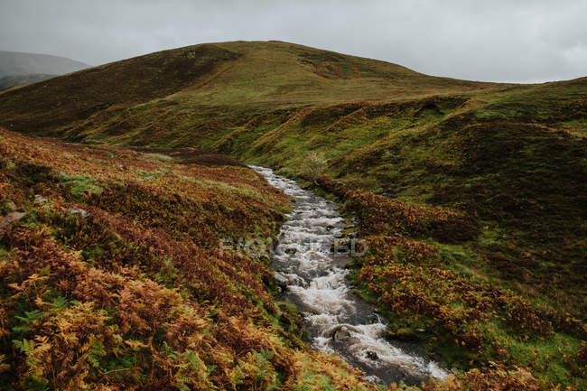 Paesaggio di torrente di montagna che attraversa le colline autunnali durante il giorno nuvoloso in Scozia — Foto stock