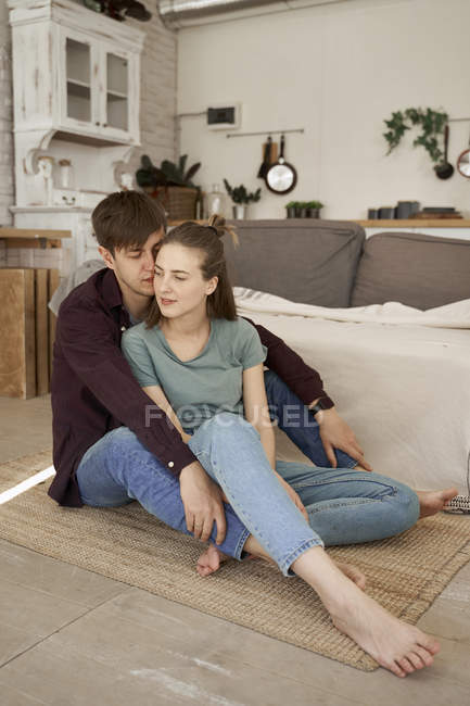 Calm charming couple embracing and enjoying as sitting barefoot on floor in cozy living room — Stock Photo