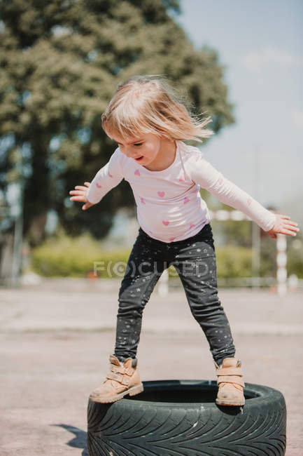 Happy joyful little girl having fun and balancing on black car tires while playing outdoors on summer day — Stock Photo