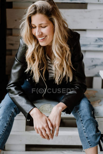 Mulher de cabelos longos na moda em jaqueta de couro e boné sentado em banco de madeira com olhos fechados — Fotografia de Stock