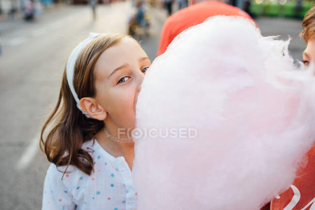 Chica alegre comiendo algodón de azúcar en la calle - foto de stock