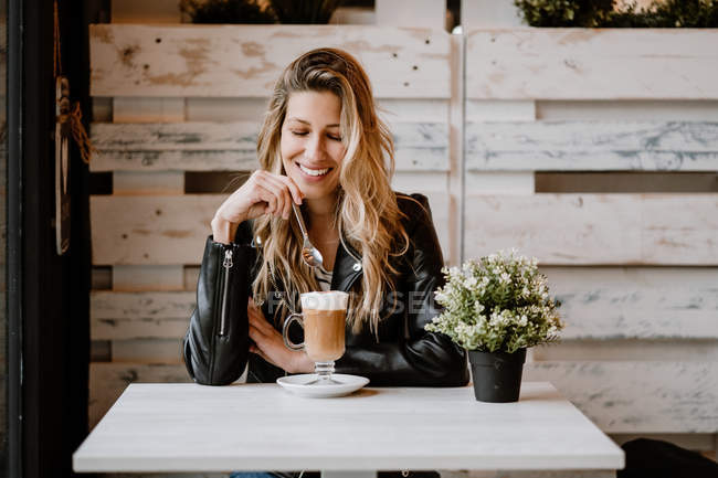 Long haired trendy beautiful blonde woman drinking from a glass of delicious foamy coffee with closed eyes — Stock Photo