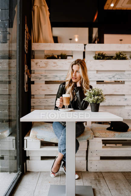 Longo cabelo na moda bela mulher loira bebendo de um copo de delicioso café espumoso enquanto olha para longe — Fotografia de Stock
