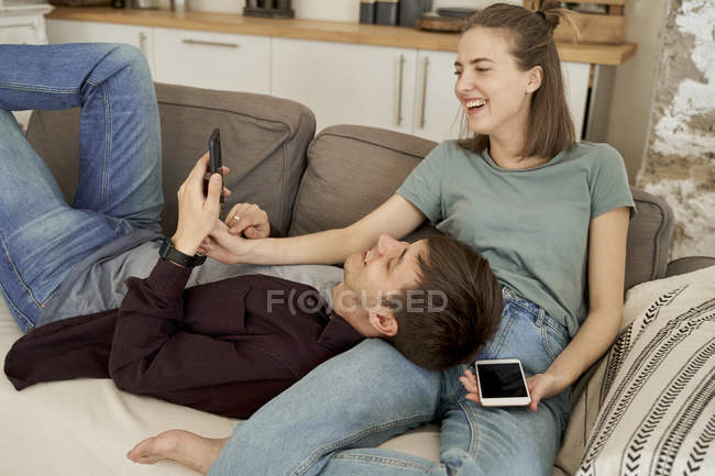Tranquilo hombre y mujer joven reflexivo acostado en el sofá suave y acogedor surf teléfonos móviles en casa - foto de stock