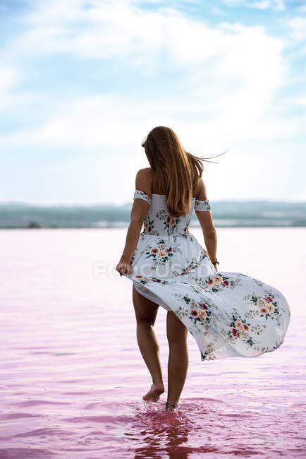 Vista posteriore della donna in abito fluente dolce camminare in acque poco profonde del lago rosa esotico a Torrevieja in Spagna — Foto stock