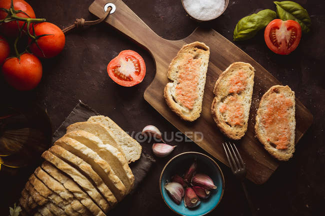 Шматочки свіжого хліба кладуть на стіл біля свіжих помідорів і часнику на столі — стокове фото