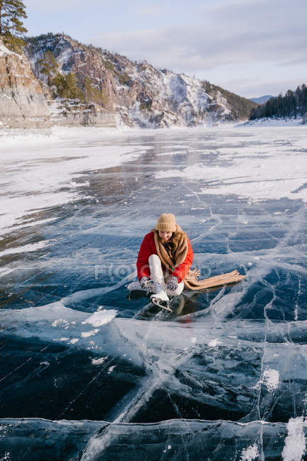 Woman sitting on frozen river and tying the shoelaces — Stock Photo